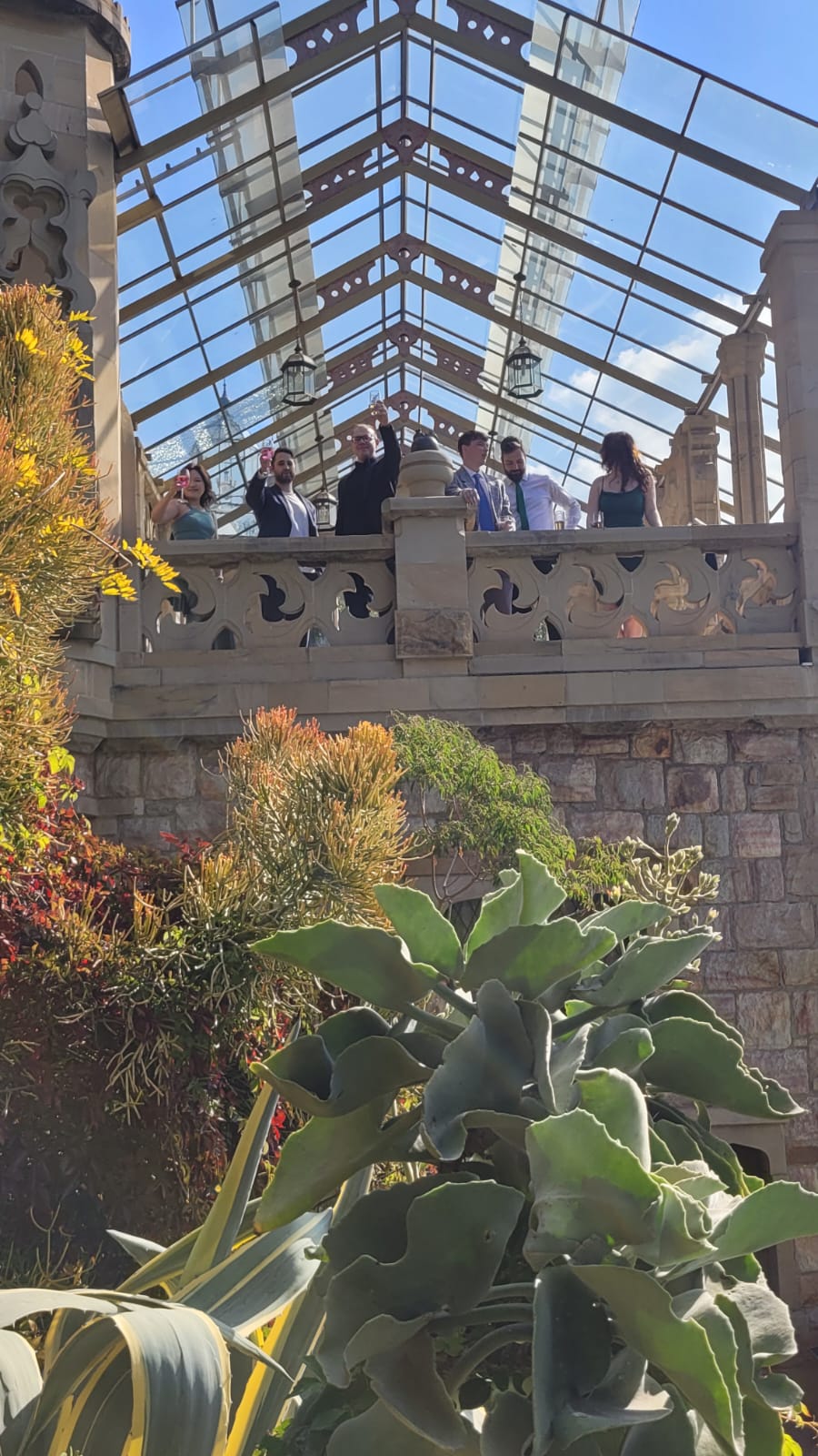 Guests raising glasses from a stone balcony beneath a glass roof
