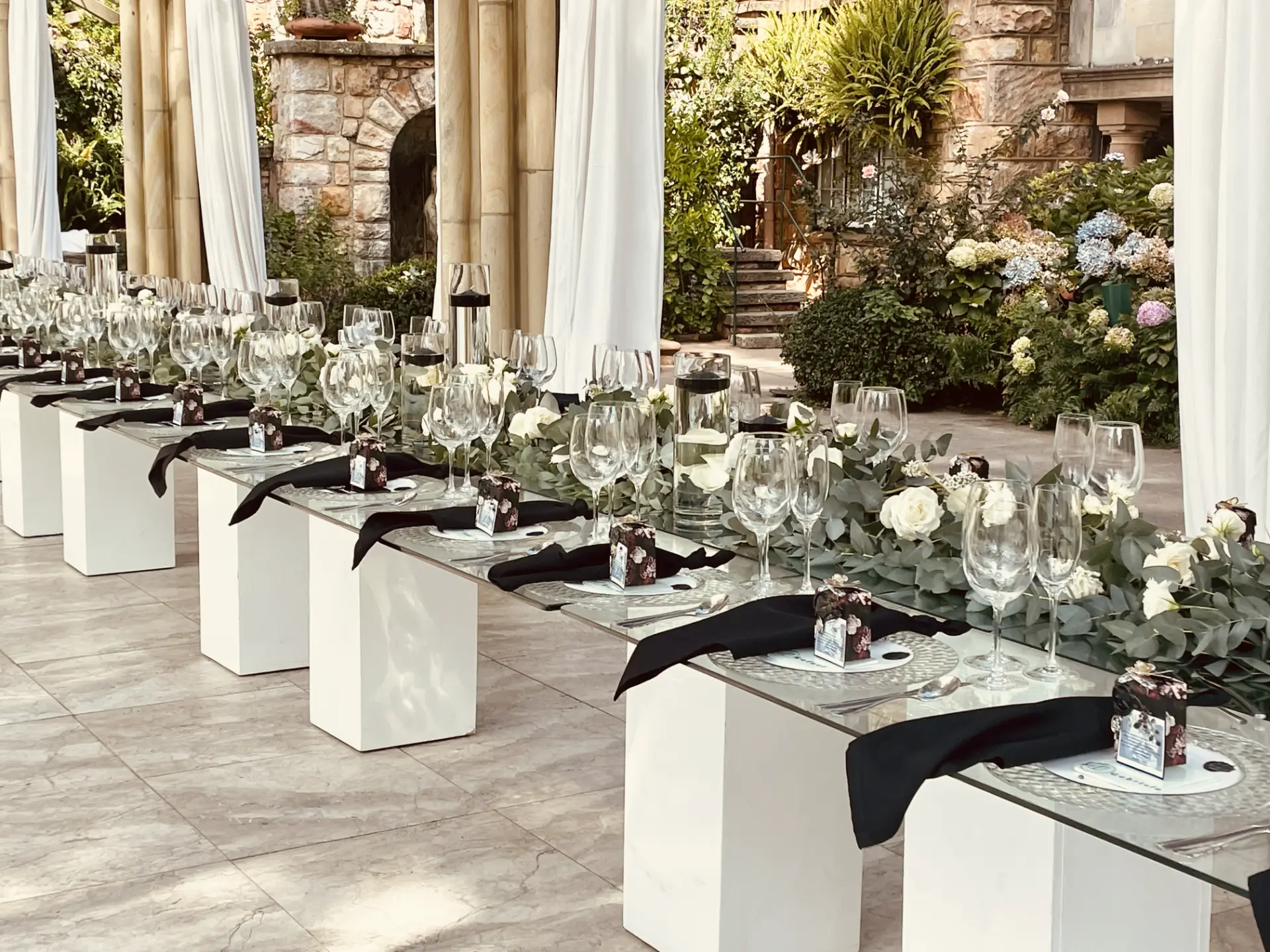 Long reception table set with glassware, white roses and black napkins