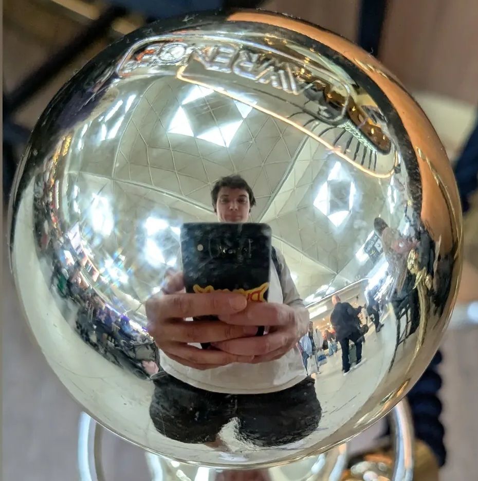 A person photographing their reflection in a polished silver sphere
